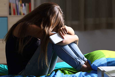Teenage girl hiding head while holding phone