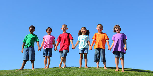 Young children standing on the grass holding hands against a blue sky